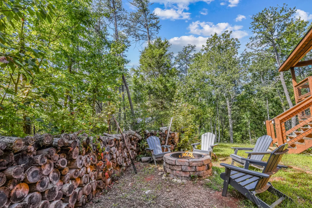 A cozy fire pit is encircled by wooden seating and backed by a rustic stone wall, offering a communal outdoor space perfect for evening gatherings, storytelling, and making s’mores under the open sky.