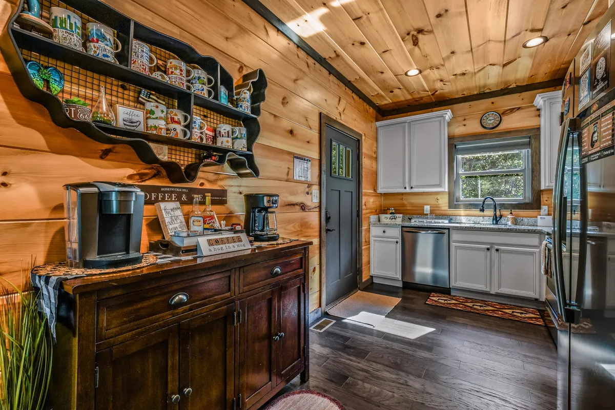 A dedicated coffee station with a wooden shelf displaying mugs, coffee machine, and kitchen appliances, all set within warm wooden cabinetry. The area feels inviting and perfect for morning rituals or casual gatherings.