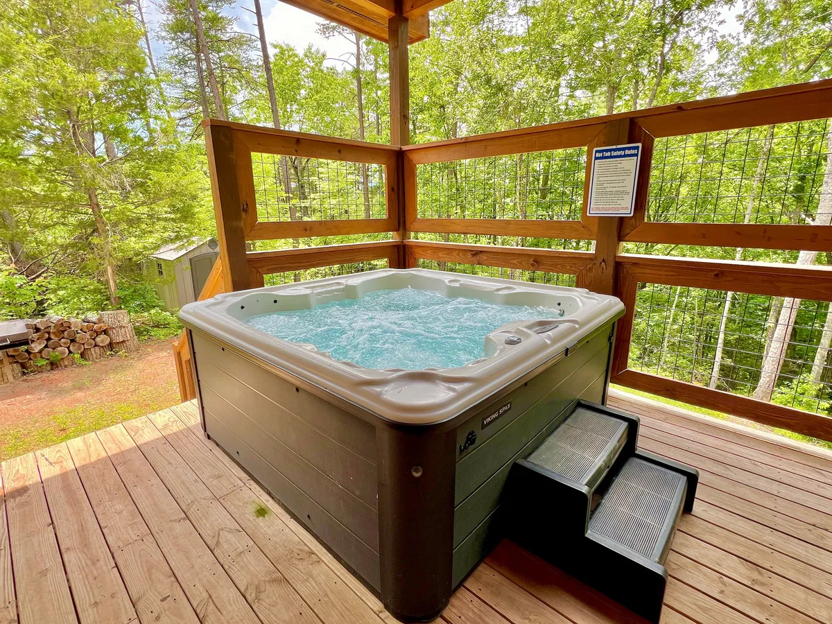 An inviting outdoor scene shows a bubbling hot tub on a spacious wooden deck, surrounded by lush greenery. The hot tub is positioned for privacy and scenic enjoyment, reinforcing a tranquil post-adventure environment.