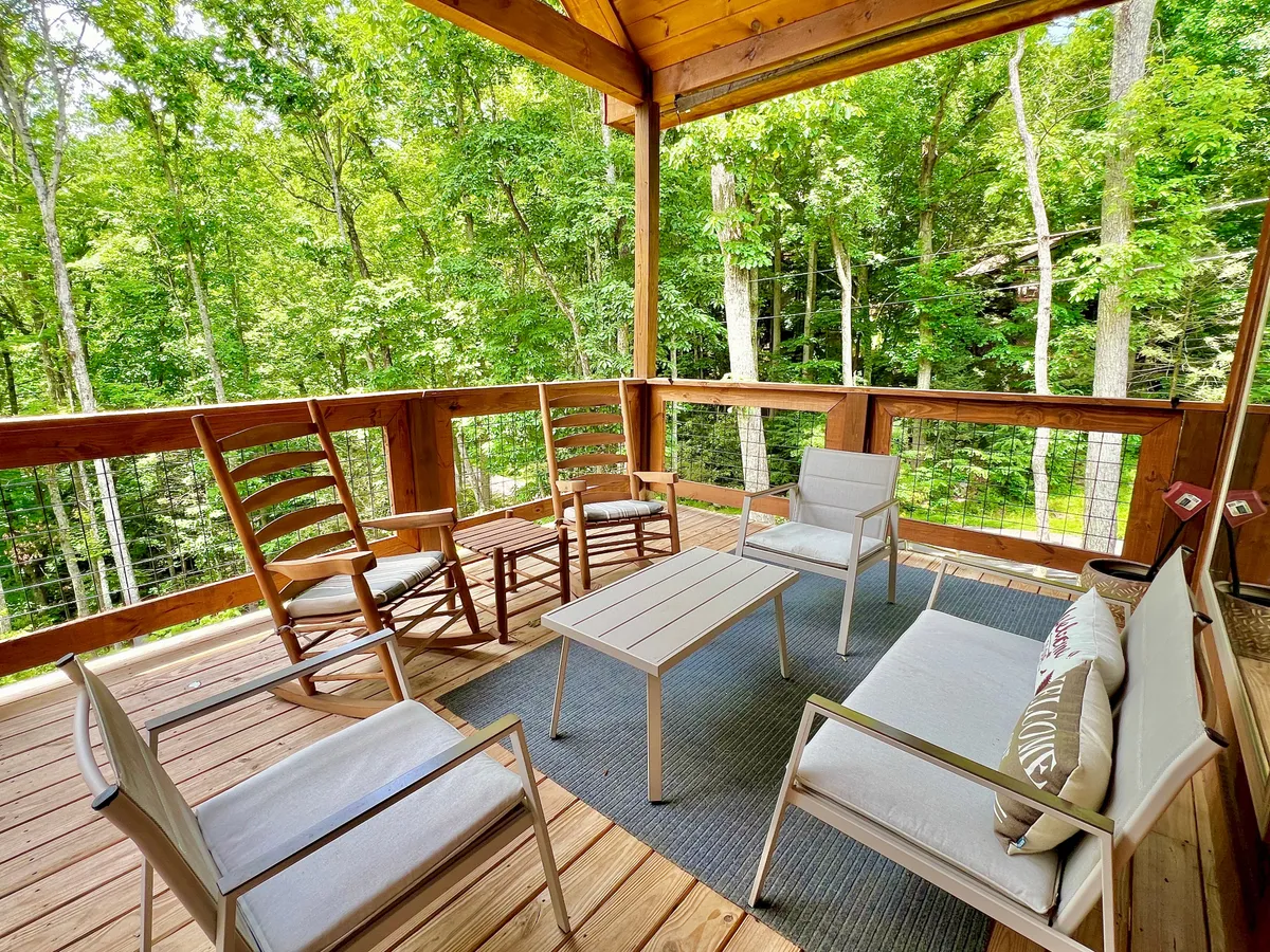 An exterior deck scene with rocking chairs, modern seating, a coffee table, and lush greenery all around. The deck invites morning coffee, sunset views, and intimate conversations amidst nature.