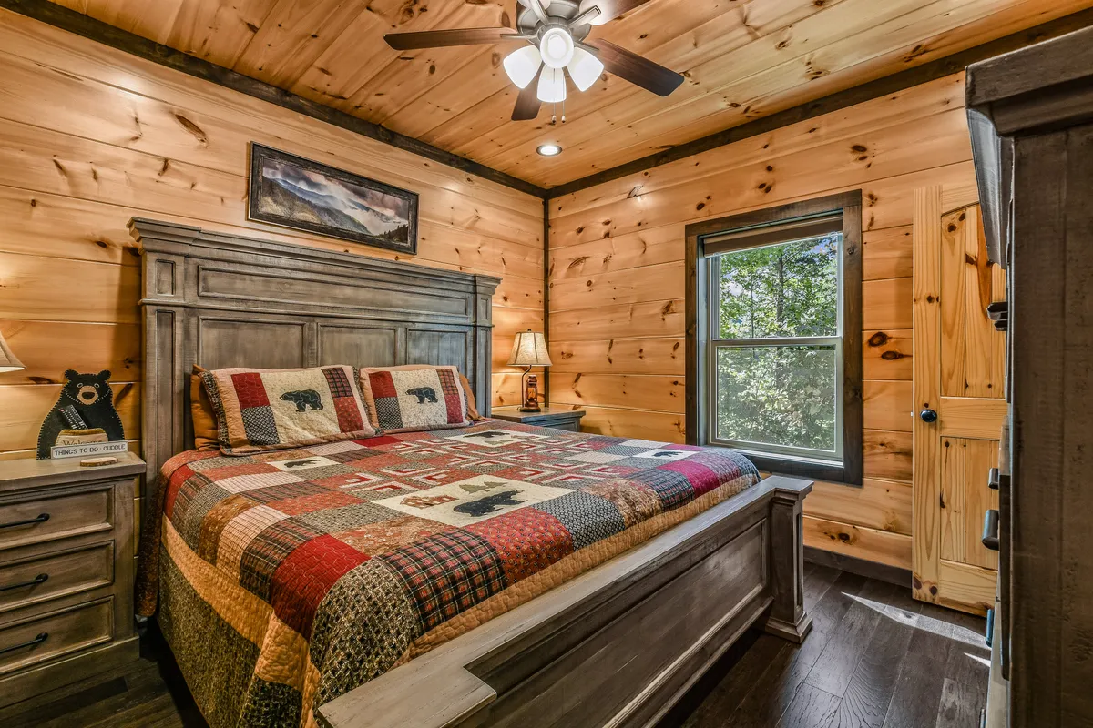 A cozy bedroom with a comfortable bed dressed in a quilt, warm wooden furniture, a soft lamp on the nightstand, and a window letting in natural light. The room exudes a serene, restful atmosphere ideal for relaxing after a day of adventure.