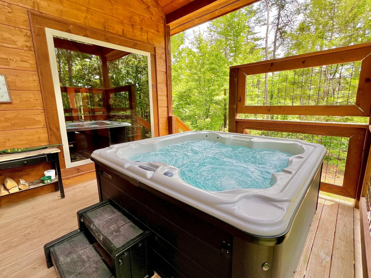 The image captures a bubbling hot tub set on a wooden structure surrounded by lush greenery, blending relaxation with the natural beauty of the Smoky Mountains. The tranquil scene invites guests to soak and unwind while taking in the peaceful outdoors.