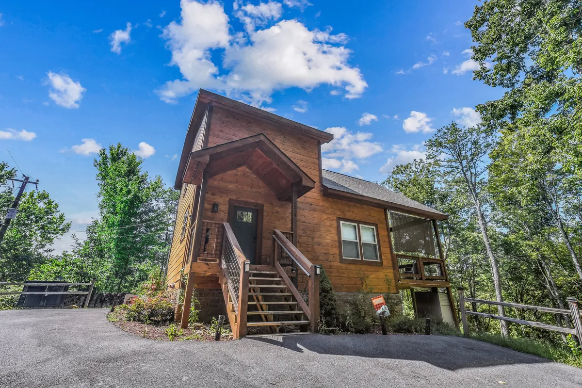 This exterior image showcases the inviting wooden cabin facade, front porch, and surrounding trees—clearly illustrating the stand-alone cabin’s privacy within the natural beauty of Sky Harbor resort. The visible staircase and level entry highlight the easy, accessible arrival mentioned in the section.