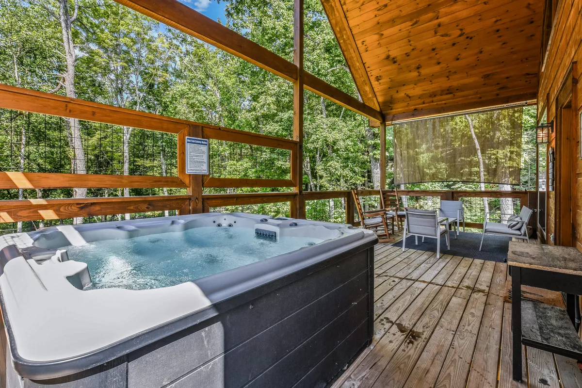 A close-up of the hot tub on the wooden deck, with seating area and lush trees in the background. The scene feels secluded and serene, ideal for couples seeking relaxation and a touch of nature.